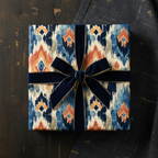 Modern ikat pattern wrapping paper in blue, orange, and cream, tied with a luxurious navy velvet ribbon, perfect for any special occasion.