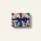 Luxury ikat pattern wrapping paper with blue and orange tones, tied with an elegant navy blue ribbon bow, perfect for unique gifts.