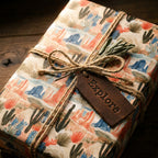 Rustic desert wrapping paper with cacti, twine bow, and leather Explore tag by Wrapped Studios.