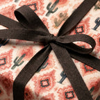 Southwest cactus wrapping paper in terracotta and green, tied with a dark brown ribbon by Wrapped Studios.