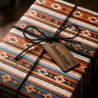 Rustic southwestern wrapping paper in orange and blue, tied with black twine and a wood tag by Wrapped Studios.