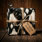 Spooky ghost wrapping paper by Wrapped Studios on a rustic Halloween gift box tied with twine.