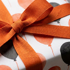 Orange and black balloon birthday wrapping paper with a matching orange ribbon bow by Wrapped Studios.