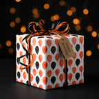 Orange and black balloon birthday wrapping paper on a gift box with ribbon and tag by Wrapped Studios.