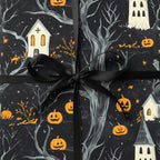 Gift wrapped in Halloween wrapping paper, featuring pumpkins, haunted houses, trees, and a black satin bow.