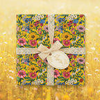 Square gift box in yellow floral wrapping paper with lace ribbon and gift tag.