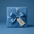 Square gift wrapped in solid blue paper with matching satin ribbon and bow, tag attached.