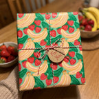 Cute fruit wrapping paper with strawberries and bananas by Wrapped Studios, tied with red twine.