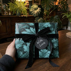 Luxury dark green botanical wrapping paper with a black velvet bow and 'With Love' tag by Wrapped Studios.