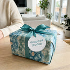 Luxury blue floral wrapping paper with teal ribbon and a Wrapped Studios tag on a gift box.