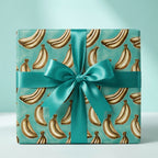 Teal banana wrapping paper on a gift box with a satin bow, perfect for unique birthday gifts. Wrapped Studios.
