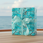 Teal marbled wrapping paper on gift box with sheer ribbon and ocean background.