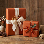 Rustic terracotta wrapping paper with white fabric ribbon and dried orange slice bow on wood table.