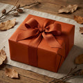 Autumn-themed gift with solid copper wrapping paper and rustic ribbon on a wooden table, perfect for fall birthdays.