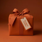 Solid copper color wrapping paper on square gift box with matching satin ribbon bow and tag.
