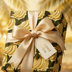 Tropical banana wrapping paper by Wrapped Studios, with a luxury cream satin bow and gift tag.