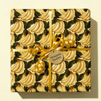 Tropical banana wrapping paper with a gold curly ribbon and a Wrapped Studios gift tag.