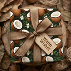 Tropical coconut wrapping paper with dark green leaves, burlap bow, and "Warm Wishes" wood tag. Rustic gift wrap.