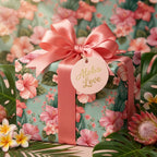 Tropical floral wrapping paper with pink hibiscus, satin bow, and "Aloha Love" tag by Wrapped Studios.