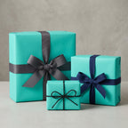Three teal presents wrapped with ribbons: gray grosgrain, navy satin, and thin black twine.