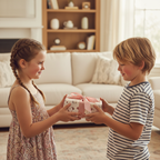 Two happy children exchange a lovely birthday gift wrapped in cute pink and white paper with a satin ribbon bow.