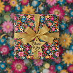 Square gift wrapped in colorful floral wrapping paper with gold ribbon and "Cheers & Joy" tag.