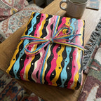 Funky gift wrap with wavy black, pink, blue, and yellow stripes tied with a raffia bow.
