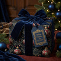 Elegant Christmas gift wrap with navy velvet ribbon, featuring red and gold ornament pattern.