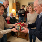 Family exchanging gift in elegant green Christmas wrapping paper with red and gold bow. Wrapped Studios.