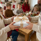 Silver luxury Christmas wrapping paper with a gold bow by Wrapped Studios, being shared at a holiday dinner.