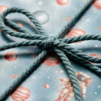 Astronaut space wrapping paper with planets and a green rope bow. Kids birthday gift wrap by Wrapped Studios.