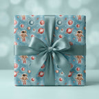 Kids outer space wrapping paper with astronauts and planets, tied with a blue satin bow by Wrapped Studios.