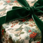 Vintage Christmas wrapping paper with winter birds and berries, tied with a green velvet bow by Wrapped Studios.