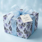 Elegant lavender floral wrapping paper with a light blue bow and 'With Love' gift tag, by Wrapped Studios.