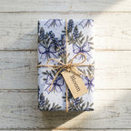 Lavender floral wrapping paper with twine and a Bloom tag on rustic wood, by Wrapped Studios.