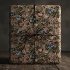 Elegant gift wrapped in vintage floral wrapping paper with brown twine on rustic wood.