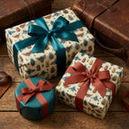 Wrapped gifts with entomology wrapping paper, teal and rust ribbons, on a wood surface with vintage suitcases.