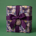 Elegant purple and gold butterfly wrapping paper with a dark purple ribbon bow from Wrapped Studios.
