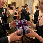 Couple exchanging luxury floral wrapping paper with a purple velvet bow at a party. Wrapped Studios.