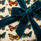 Butterfly print birthday wrapping paper with a teal velvet ribbon bow, elegant gift wrap.
