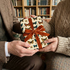 Hands exchanging a gift wrapped in butterfly patterned wrapping paper with velvet ribbon.