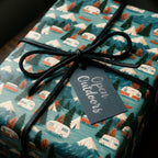 Rustic camping wrapping paper with mountains and trailers, tied with a black bow by Wrapped Studios.
