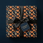 Celestial wrapping paper with a mystical sun and moon pattern, tied with a black satin bow by Wrapped Studios.
