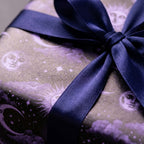 Mystical celestial wrapping paper with purple sun and moon pattern and navy satin bow by Wrapped Studios.