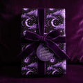 Purple celestial wrapping paper with moons and stars by Wrapped Studios, tied with a velvet bow.