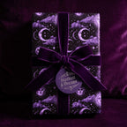Purple celestial wrapping paper with moons and stars by Wrapped Studios, tied with a velvet bow.