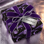 Celestial wrapping paper with purple sun and moon pattern, velvet bow, and silver tag by Wrapped Studios.