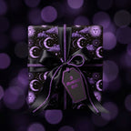 Gothic celestial wrapping paper with purple suns, moons, black ribbon, and coffin tag by Wrapped Studios.