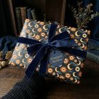Mystical celestial wrapping paper with a sun and moon pattern and blue velvet bow by Wrapped Studios.