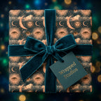 Luxury celestial wrapping paper featuring gold moons and eyes, tied with a teal velvet bow by Wrapped Studios.